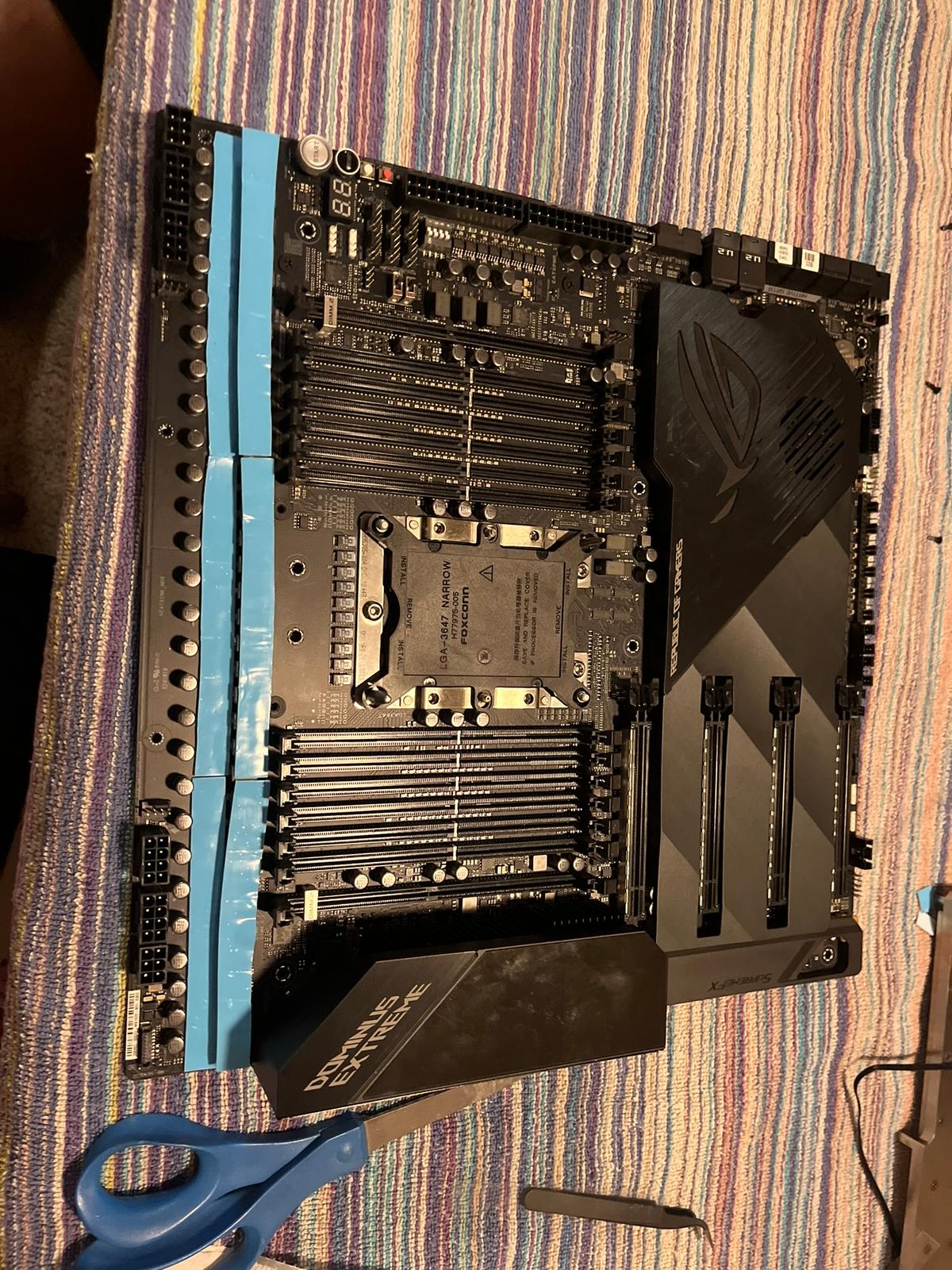 ROG Dominus Extreme laid flat on the bench — thermal pad material laid over the full VRM array, scissors on standby, LGA 3647 socket visible
