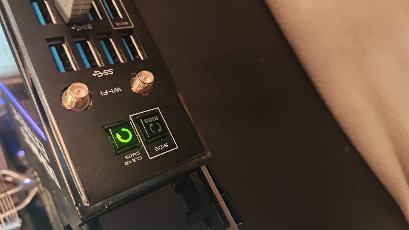 Rear I/O close-up — Clear CMOS button glowing green, BIOS reset button below it